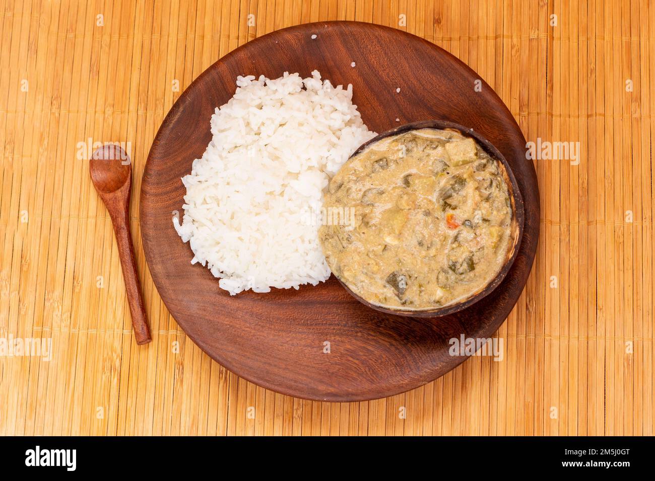 Traditioneller afrikanischer Grünkohl-Eintopf mit Kokosmilch und Erdnussmehl, serviert in einer Kokosnussschale mit weißem Reis: Ein köstliches und nahrhaftes Gericht aus Moza Stockfoto