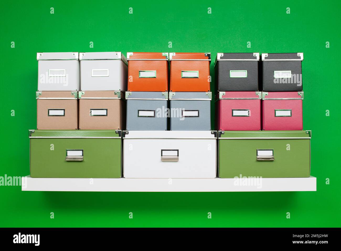 Ordentliche Reihen von Boxen in verschiedenen Farben und Größen auf einem weißen Bücherregal an einer grünen Wand. Minimalistische Zusammensetzung zum Thema Organisation Stockfoto