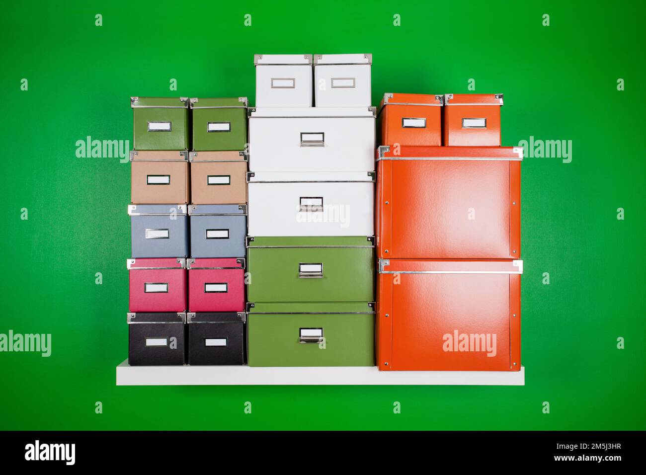 Hoher Stapel von Bürokartons in verschiedenen Farben und Größen auf einem weißen Bücherregal an einer grünen Wand. Minimalistische Kompostierungszusammensetzung Stockfoto