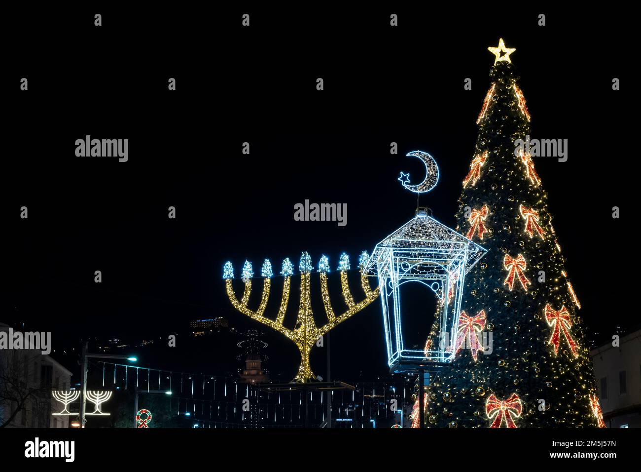 Ein dekorierter Weihnachtsbaum mit beleuchteter Menorah Hanukkah und dem Halbmond des Neumunds, der mit dem Islam assoziiert ist, wird im deutschen Kolonialviertel in Haifa, Israel, gezeigt, während die Stadt den Feiertag feiert, der die Feiertage in Hanukka, Weihnachten und Ramadan der drei großen Religionen kennzeichnet: Christentum, Judentum und Islam. Stockfoto