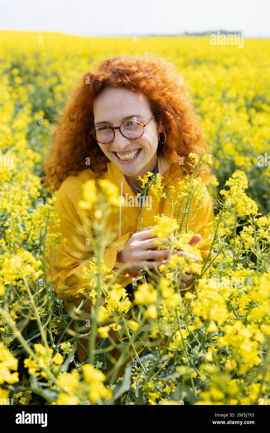 Eine weiße Frau, die auf einem Feld gelber Blumen lächelt Stockfoto