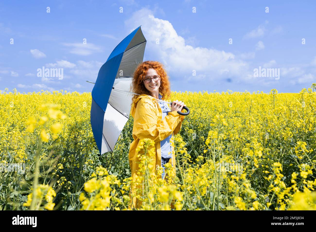 Junge Frau, die mit einem blauen Regenschirm posiert, an einem warmen Frühlingstag Stockfoto