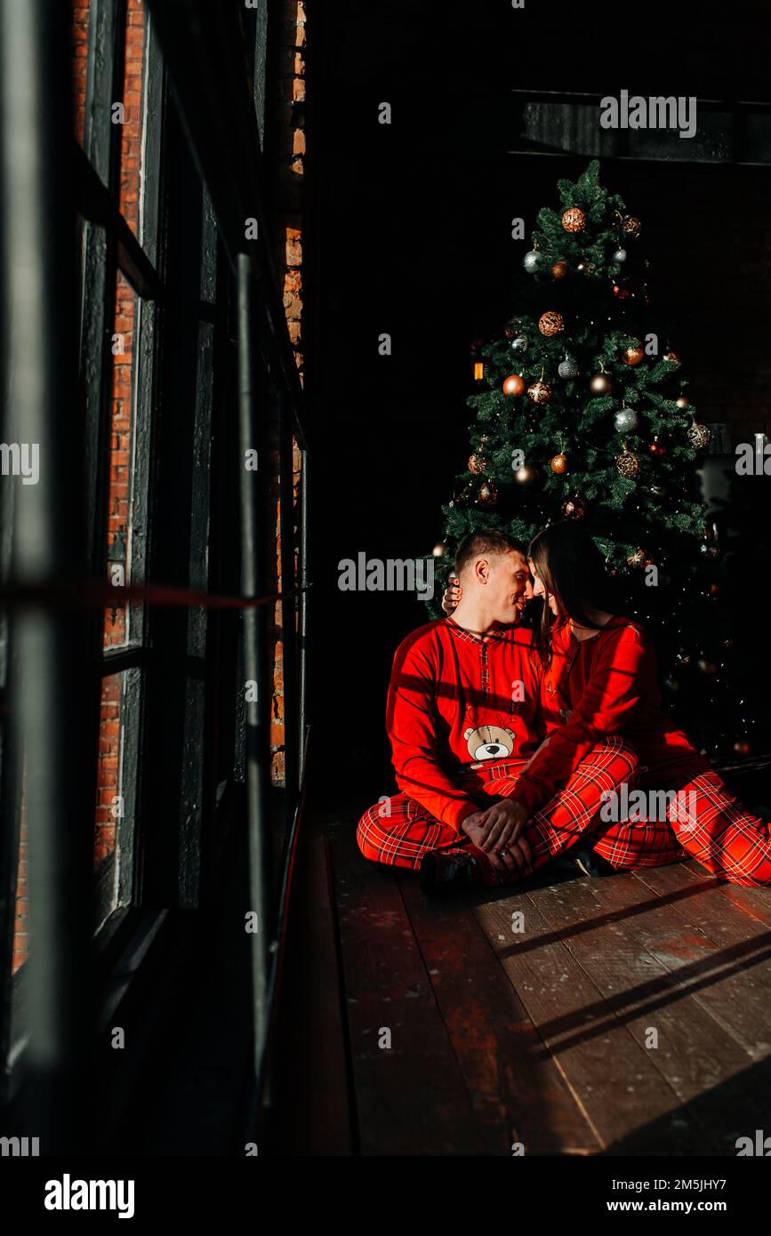Attraktiver, fröhlicher Mann und Frau, die neben dem Weihnachtsbaum sitzen. Stockfoto