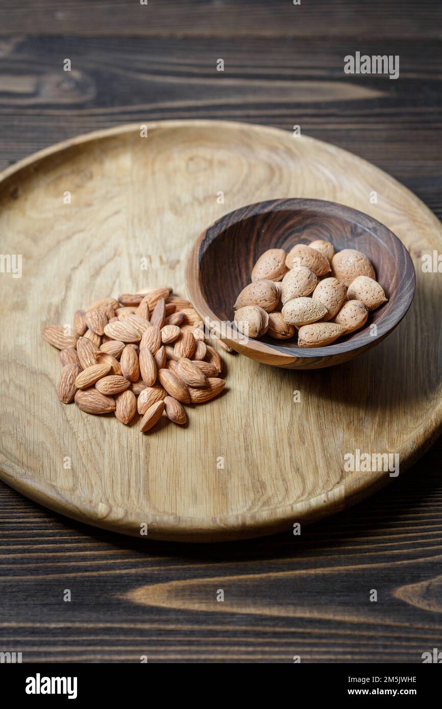 Geschälte rohe Mandeln auf einer Holzplatte und Mandeln in einer Schale in einer Holzschüssel auf einem Holzhintergrund. NUTS-, Ernährungs- und Rohnahrungskonzept Stockfoto