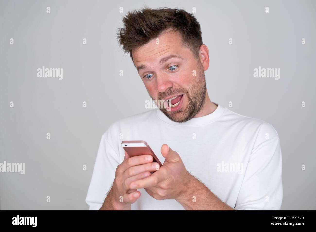 Ein Mann, der auf den Bildschirm des Smartphones schaut und beim Chatten mit einem Freund freundlich lächelt Stockfoto