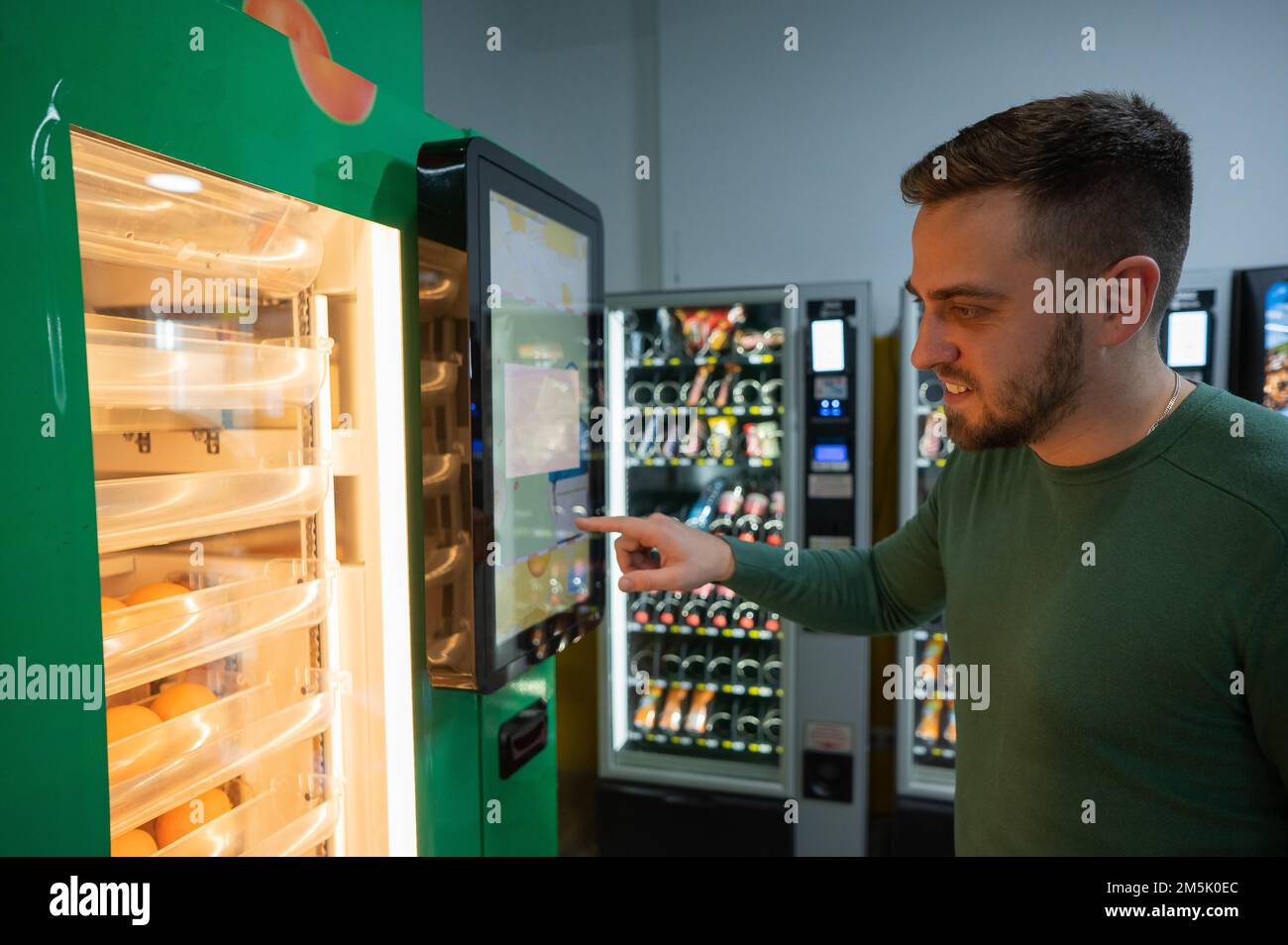 Ein weißer Mann kauft frisch gepressten Orangensaft aus dem Automaten. Stockfoto