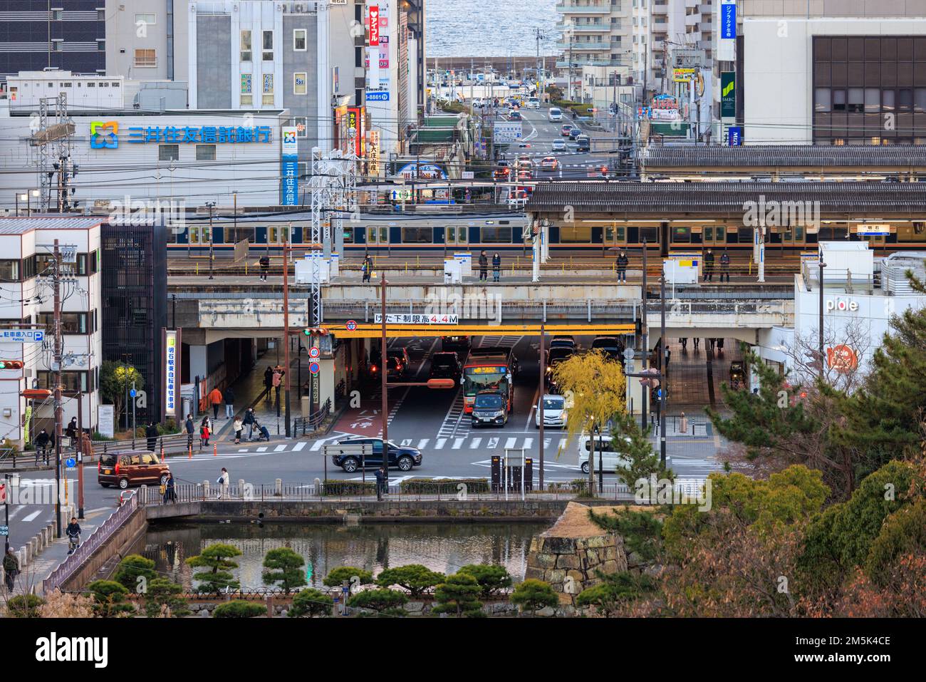 Akashi, Japan - 29. Dezember 2022: Leichter Verkehr durchquert die Kreuzung in der Innenstadt, während die Züge über dem Bahnhof abfahren Stockfoto