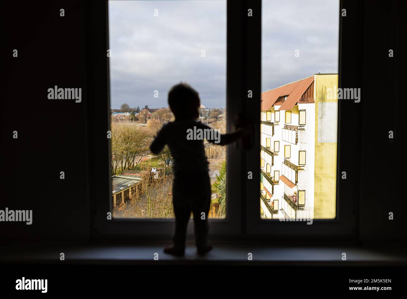 Einsames Kind, das auf dem Fensterbrett steht. Gefahrensituation, Sturzgefahr. Stockfoto