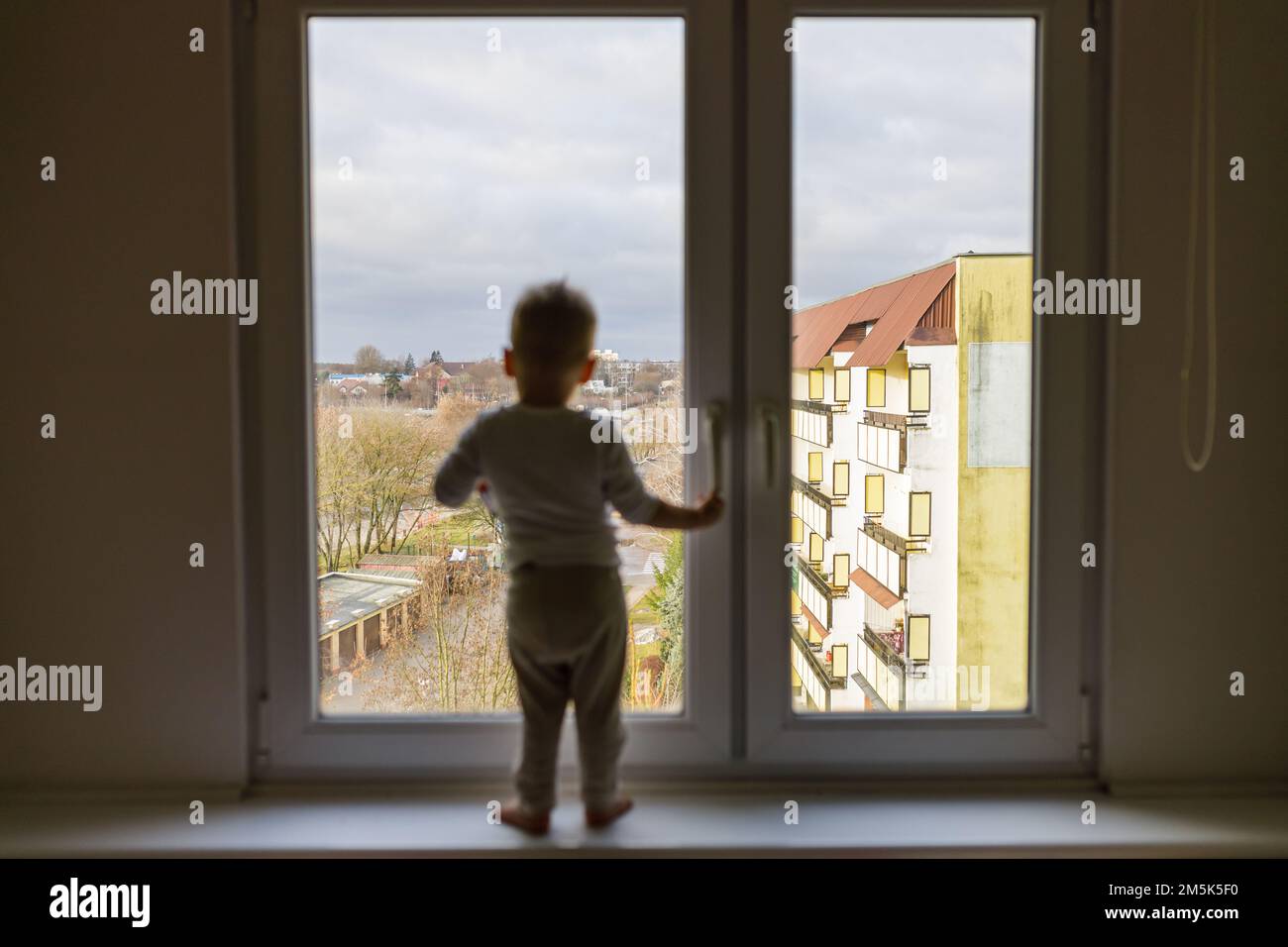Einsames Kind, das auf dem Fensterbrett steht. Gefahrensituation, Sturzgefahr. Stockfoto