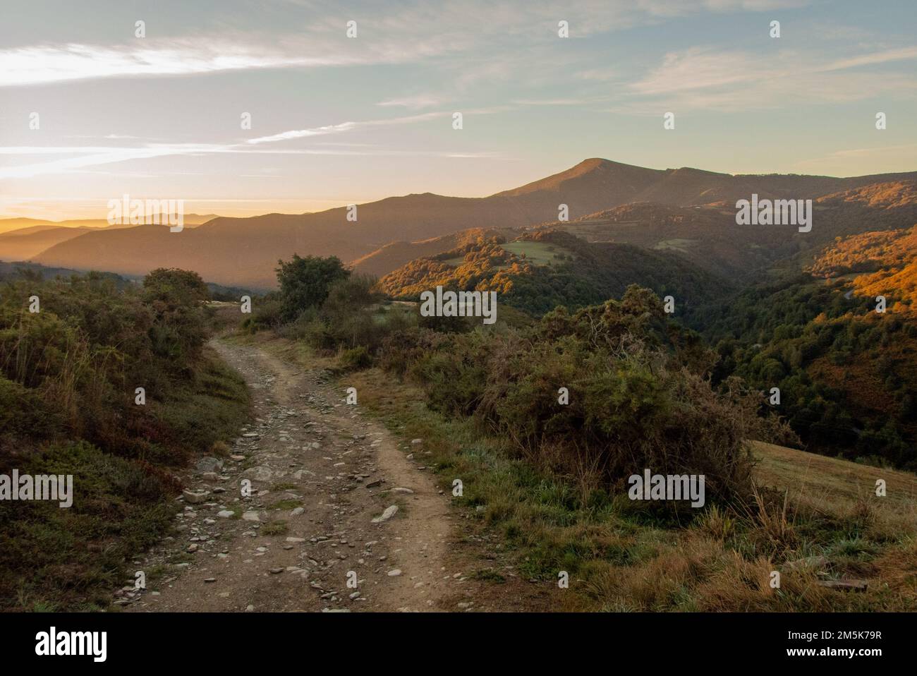 Sie verlassen La Faba auf einem rauen Teil des Camino de Santiago in die Berge von Galicien und blicken zurück auf den Sonnenaufgang über Kastilien und León. Stockfoto