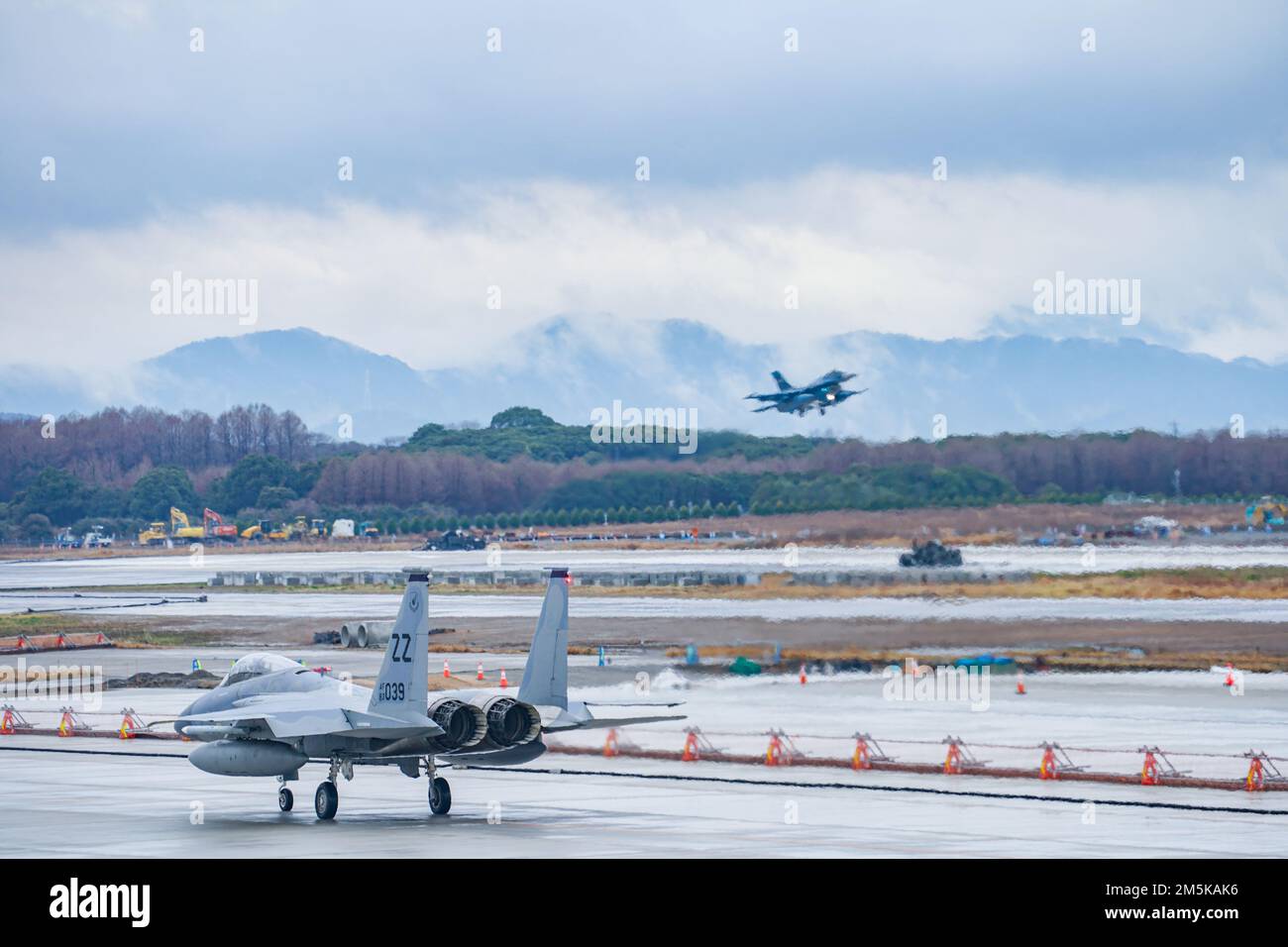 EIN US-AMERIKANISCHER Die Air Force F-15C Eagle wurde der 44. Kampfstaffel zugeteilt, Kadena Air Base, Japan, Taxis auf der Fluglinie des Tsuiki Air Base, 22. März 2022, während eine Japan Air Self-Defense Force F-2A im Hintergrund startet. Der Luftwaffenstützpunkt Tsuiki war Gastgeber des Umsiedlungsprogramms für Flugschulungen im März 2022, das die Betriebsbereitschaft verbessert und die Interoperabilität mit unseren japanischen Verbündeten verbessert. Stockfoto