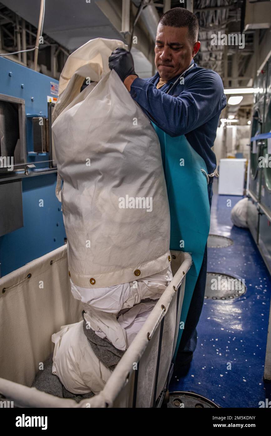 220322-N-TF178-1072 PAZIFIK (22. März 2022) – Retail Services Specialist 2. Klasse David Aviles leert einen Beutel Wäsche in einen Wagen an Bord des Amphibienschiffs USS Makin Island (LHD 8), März 22. Makin Island führt Routineeinsätze in der US-3.-Flotte durch. Stockfoto