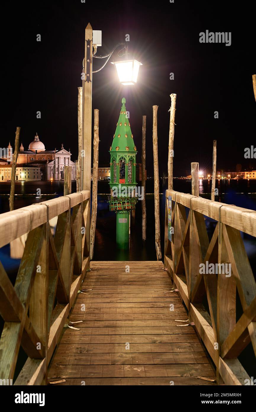 Holzpier zum Andocken venezianischer Gondeln im Dunkeln der Nacht durch Laternen Iluninadas, eine Laterne mit grünem und goldenem Hintergrund Stockfoto