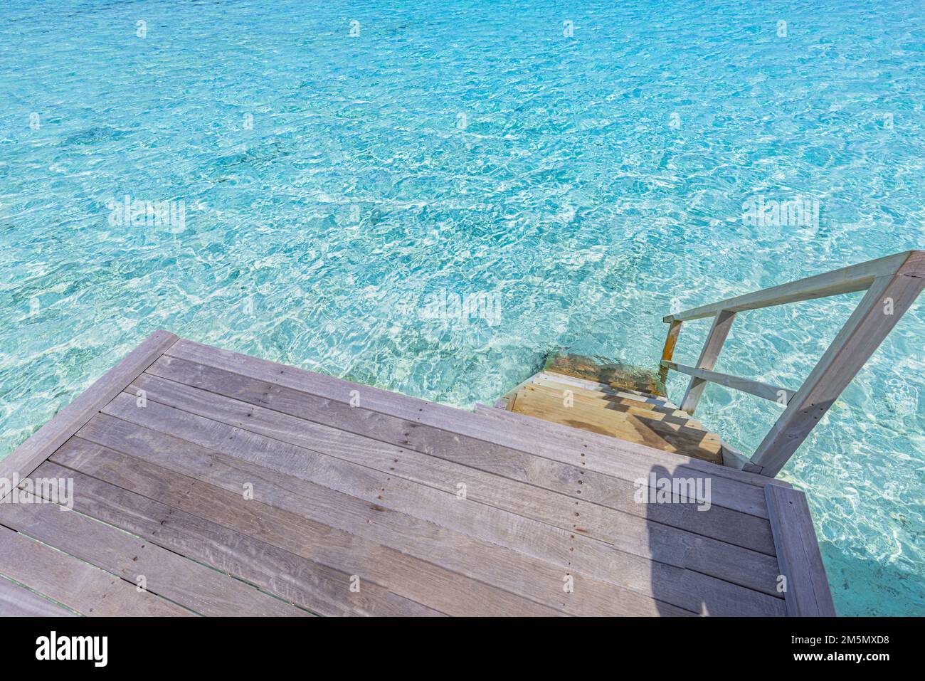Hölzerne Plattform mit Stufen zum azurblauen Meerwasser auf den Malediven. Die Treppe führt von der Überwasser-Villa zur Ozeanlagune, Sommerurlaub Stockfoto
