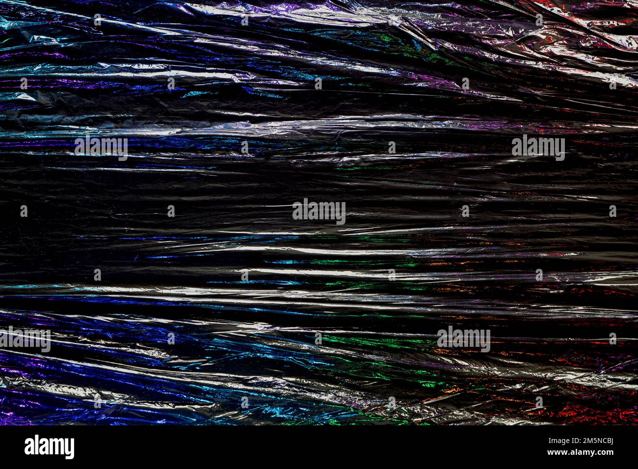 Schwarzer Hintergrund mit Kunststoffumwicklung. Dunkles, zerknittertes Plastikzellophan. Reflektiert farbenfrohes schillerndes Licht und Schatten auf Falten und Falten Stockfoto