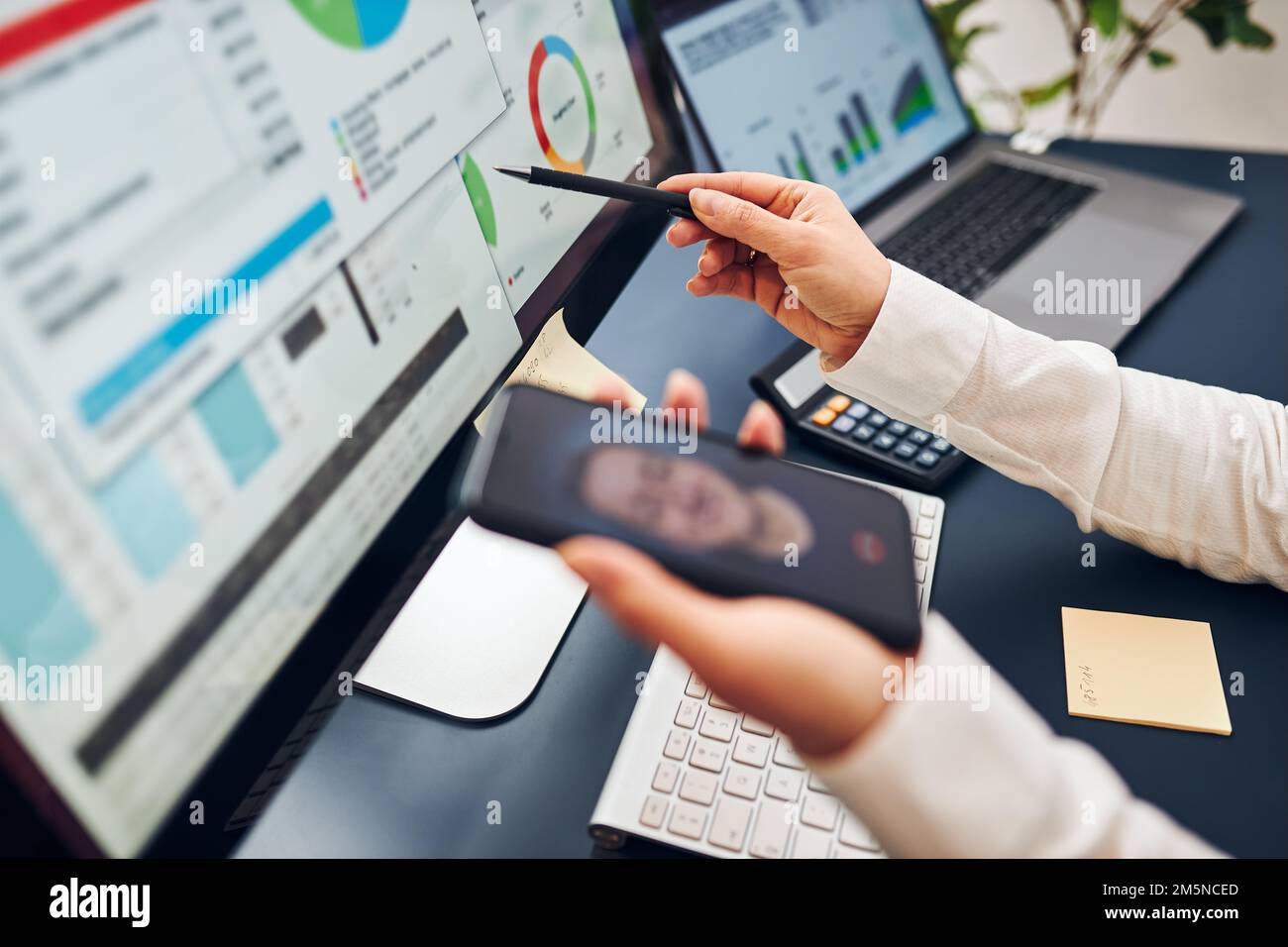 Geschäftsfrau, die mit ihrem Kollegen per Mobiltelefon Videochats führt. Geschäftsfrau, die mit Daten in Diagrammen, Diagrammen und Diagrammen auf dem Computerbildschirm arbeitet. Stockfoto