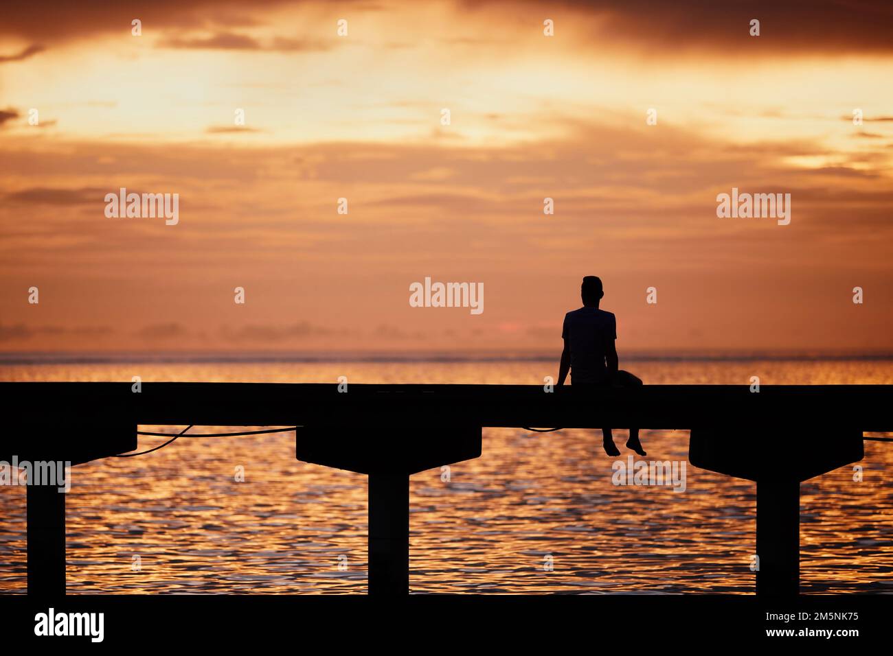 Ein Mann, der am Rande des Piers denkt und den goldenen Sonnenuntergang im Meer sieht. Stockfoto