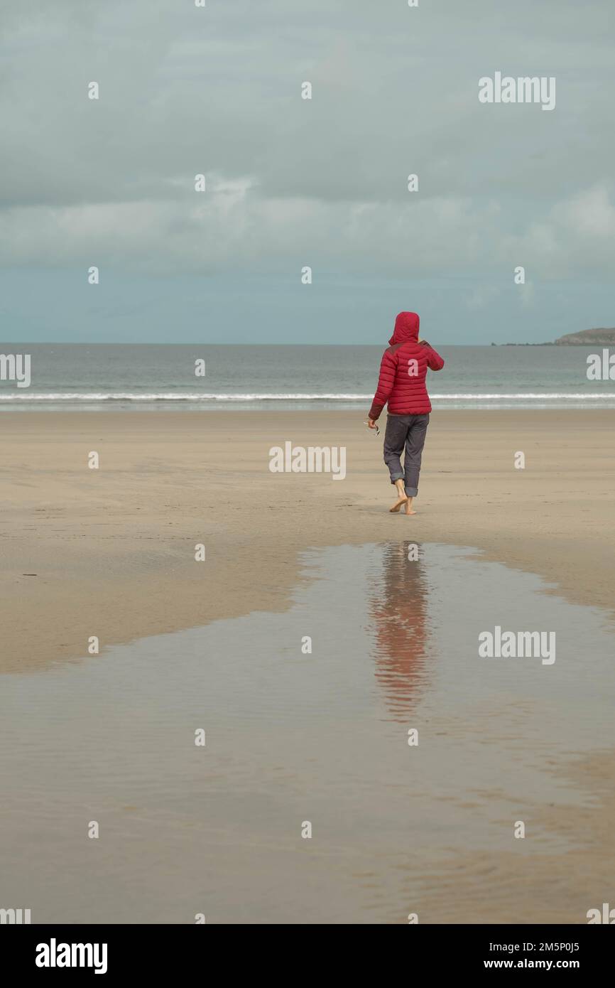Eine Frau in Rot, die an einem kalten Strand in der bretagne spaziert Stockfoto