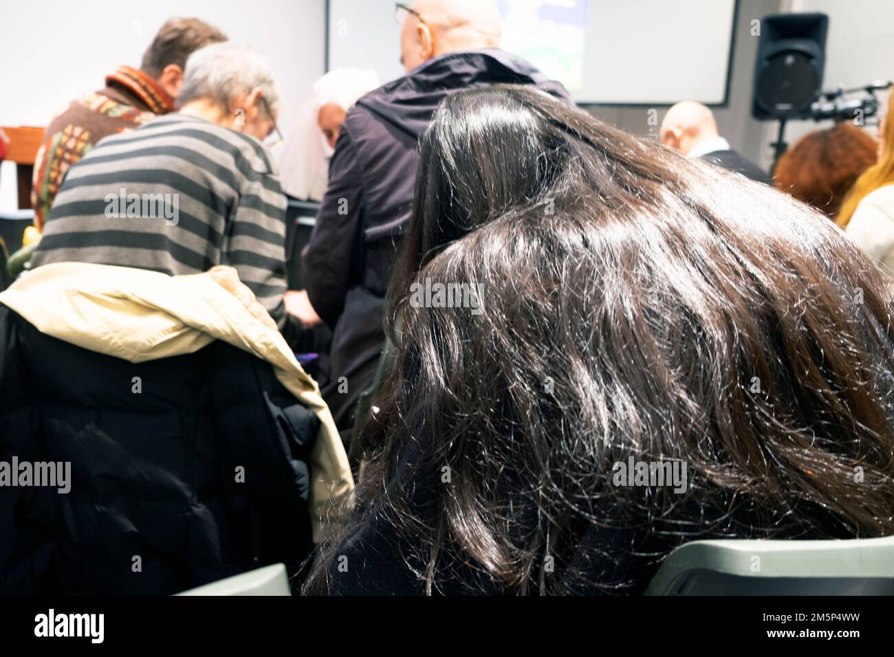 Rückansicht einer Frau mit wunderschönen langen schwarzen Haaren und einem Publikum, das in der Vorlesungshalle UK 2023 KATHY DEWITT auf Mobiltelefone schaut Stockfoto
