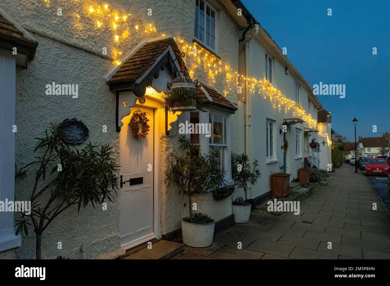 Weihnachtslichter und Kranz in der Dämmerung an Häusern in der Odiham High Street, einem Dorf in Hampshire, England, in der Dämmerung im Dezember Stockfoto