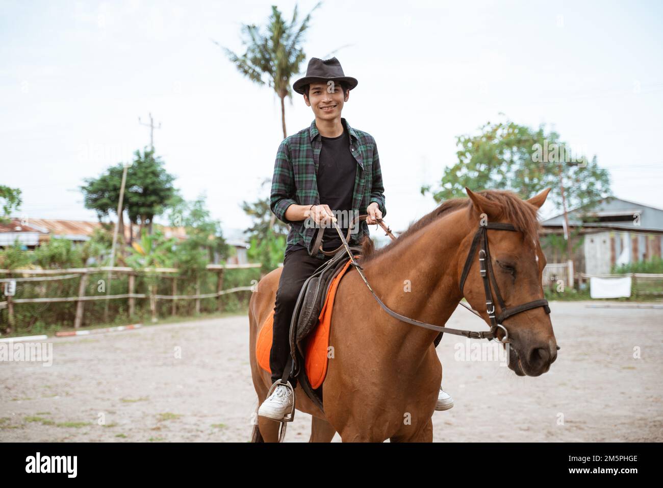 ein asiatischer Mann mit Cowboyhut, reitet auf Pferden und hält Zügel Stockfoto