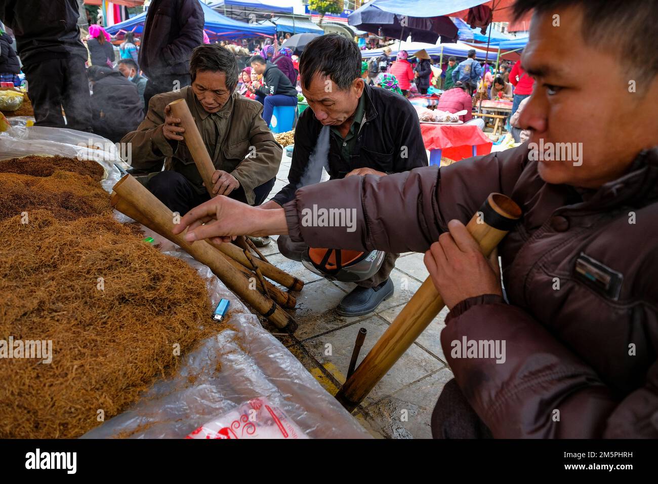 BAC Ha, Vietnam - 18. Dezember 2022: Männer, die auf dem Wochenmarkt von Bac Ha in Vietnam Tabak rauchen. Stockfoto