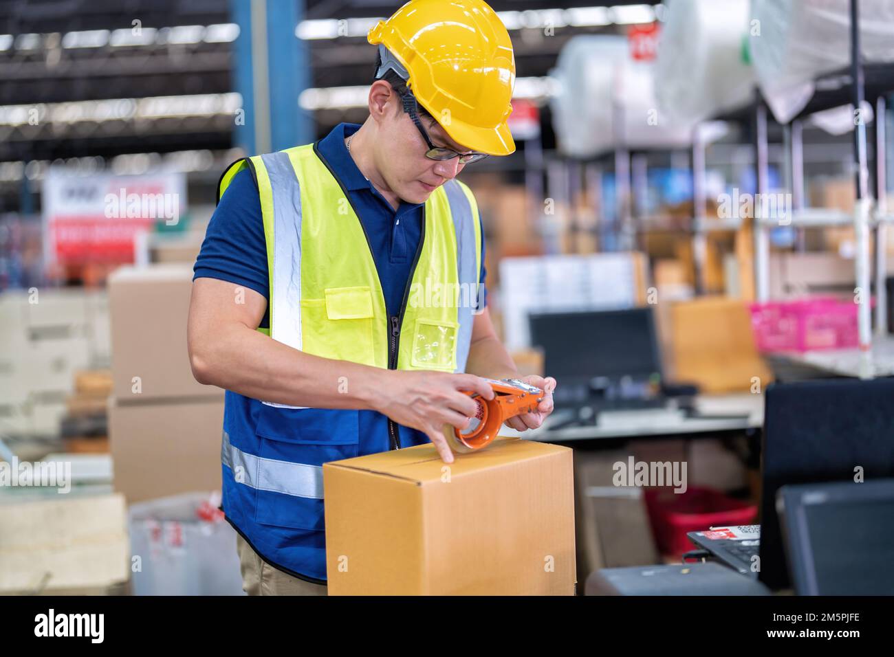 Arbeiter im großen Lagerlager verwenden Klebeband, um Verpackungskartons an der Kasse vorzubereiten Stockfoto