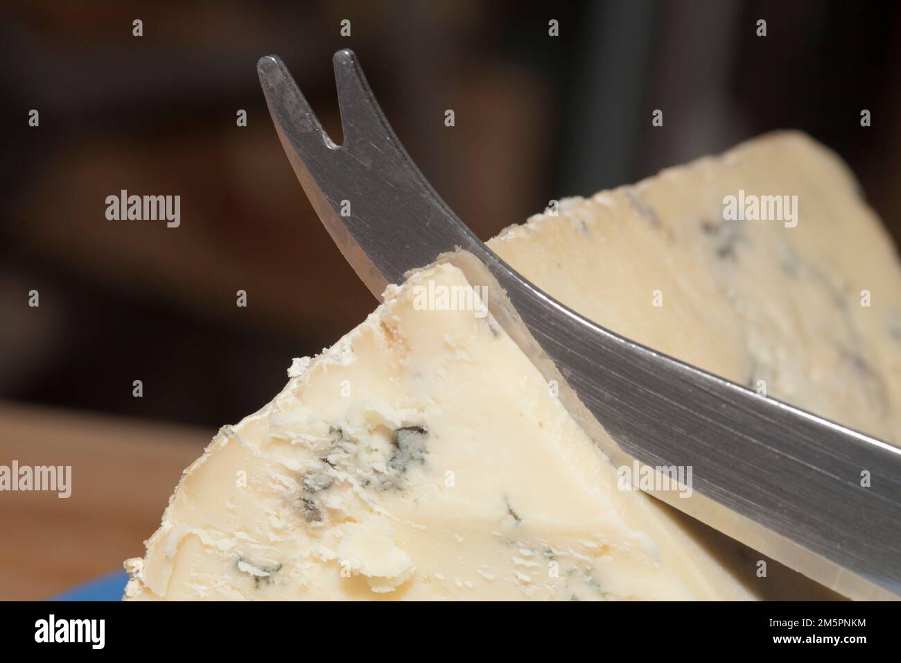 Käsemesser, das in Blauen Stilton englischen Käse auf Cornish-Besteck schneidet. Blauer und weißer Teller Stockfoto
