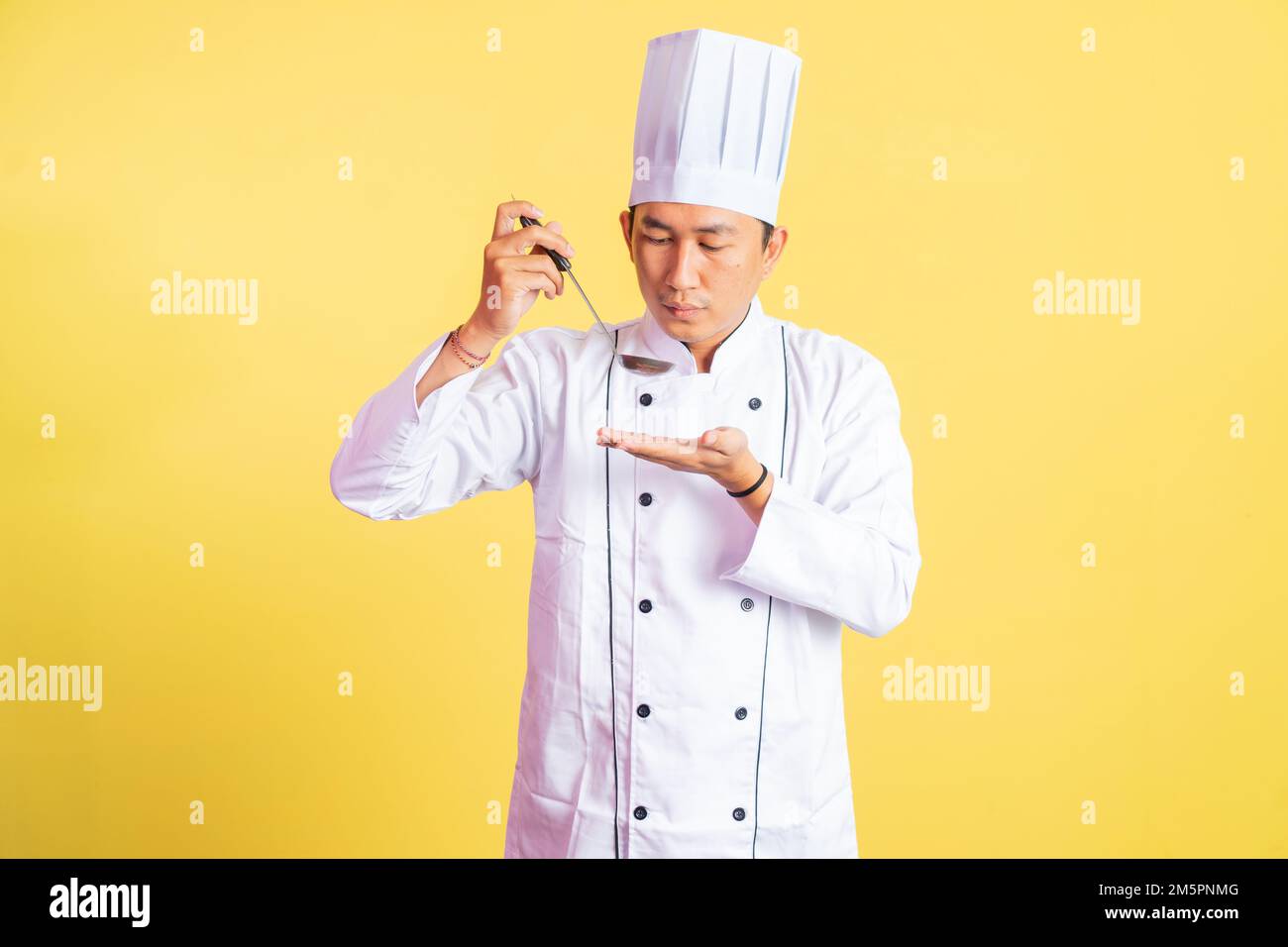 Asiatischer männlicher Koch, der warme Speisen mit einer Kelle probiert Stockfoto