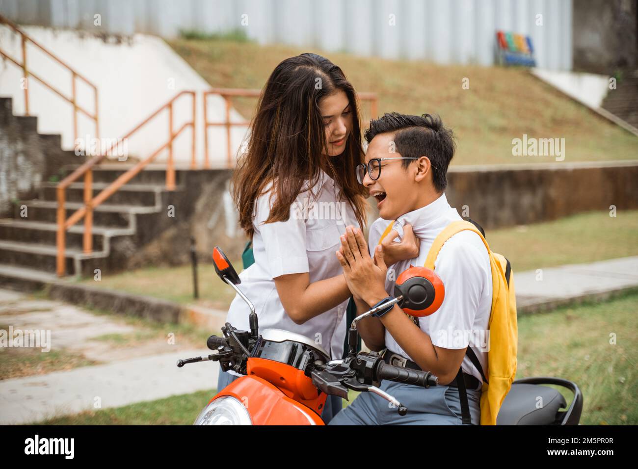 Tomboy-Mädchen-Schülerin fordert einen Jungen-Schüler heraus, während er Motorrad fährt Stockfoto