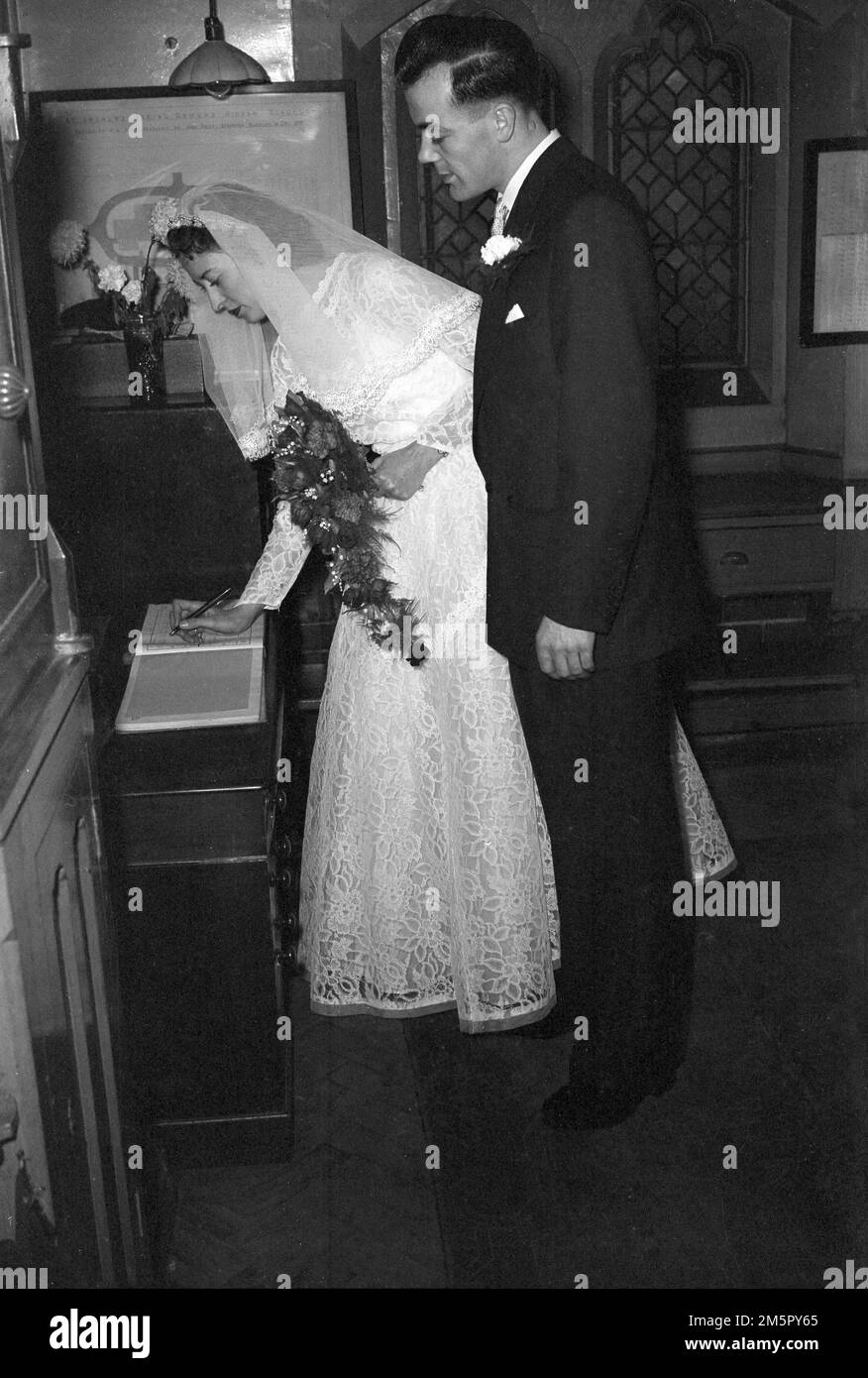 1950er Jahre, Geschichte, Braut und Bräutigam in der Kirche, die frisch verheiratete Braut unterzeichnet das Register, England, Großbritannien. Stockfoto