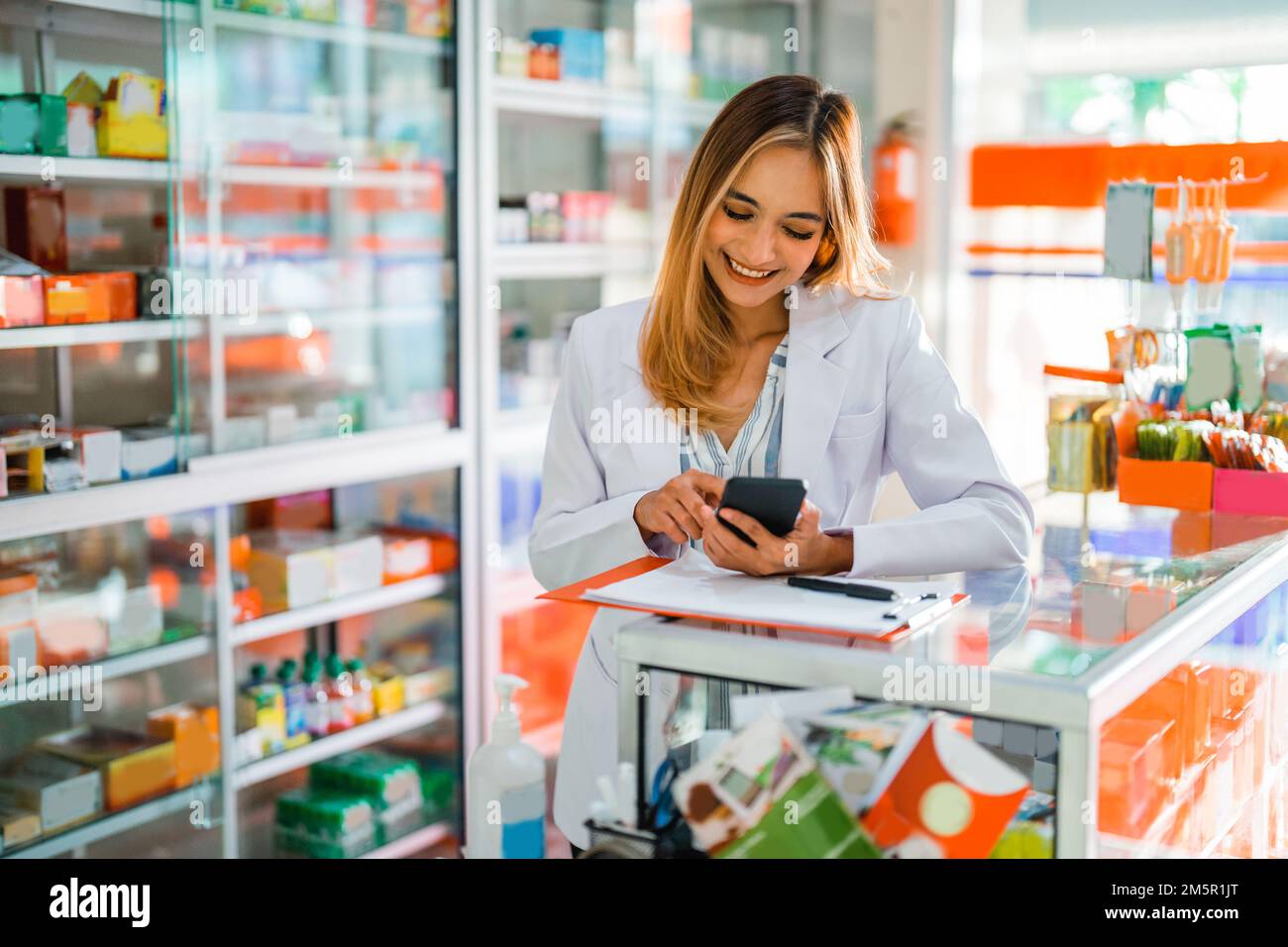 Attraktiver Apotheker in Uniform mit Smartphone während der Arbeit Stockfoto