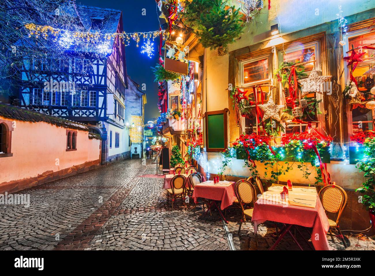 Straßburg, Frankreich. Straßencafé-Tische in der Winterstraße, Weihnachtszeit. Elsass Nacht Szene mit hervorgehoben alten Gebäuden in tourisitic Konzept. Stockfoto