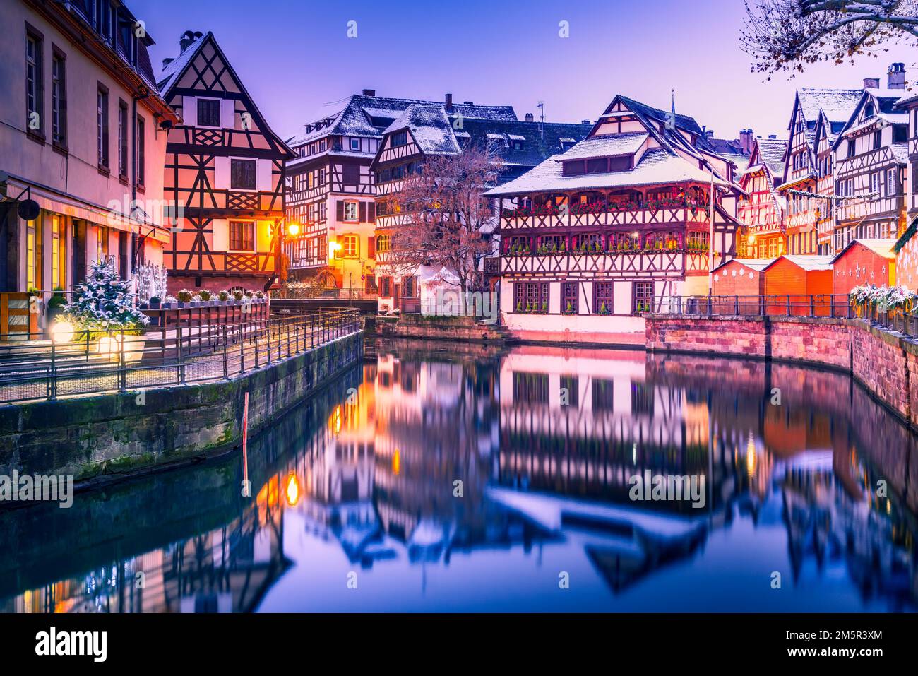Straßburg, Elsass. Traditionelle elsässische Fachwerkhäuser mit Spiegelreflexionen in Petite France während der Weihnachtszeit mit Dämmerung. Stockfoto