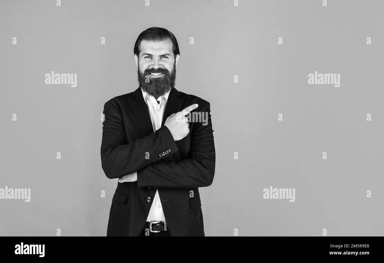 Stilvoller reifer Mann, der mit dem Finger zeigt. Herren Jacke Garderobe. Modischer Mann im Anzug. Formelles Modemodell. Ein hübscher Mann, der auf Grau steht Stockfoto