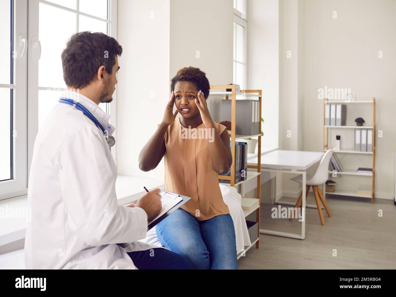 Männlicher Arzt konsultiert eine schwarze Frau mit Kopfschmerzen Stockfoto