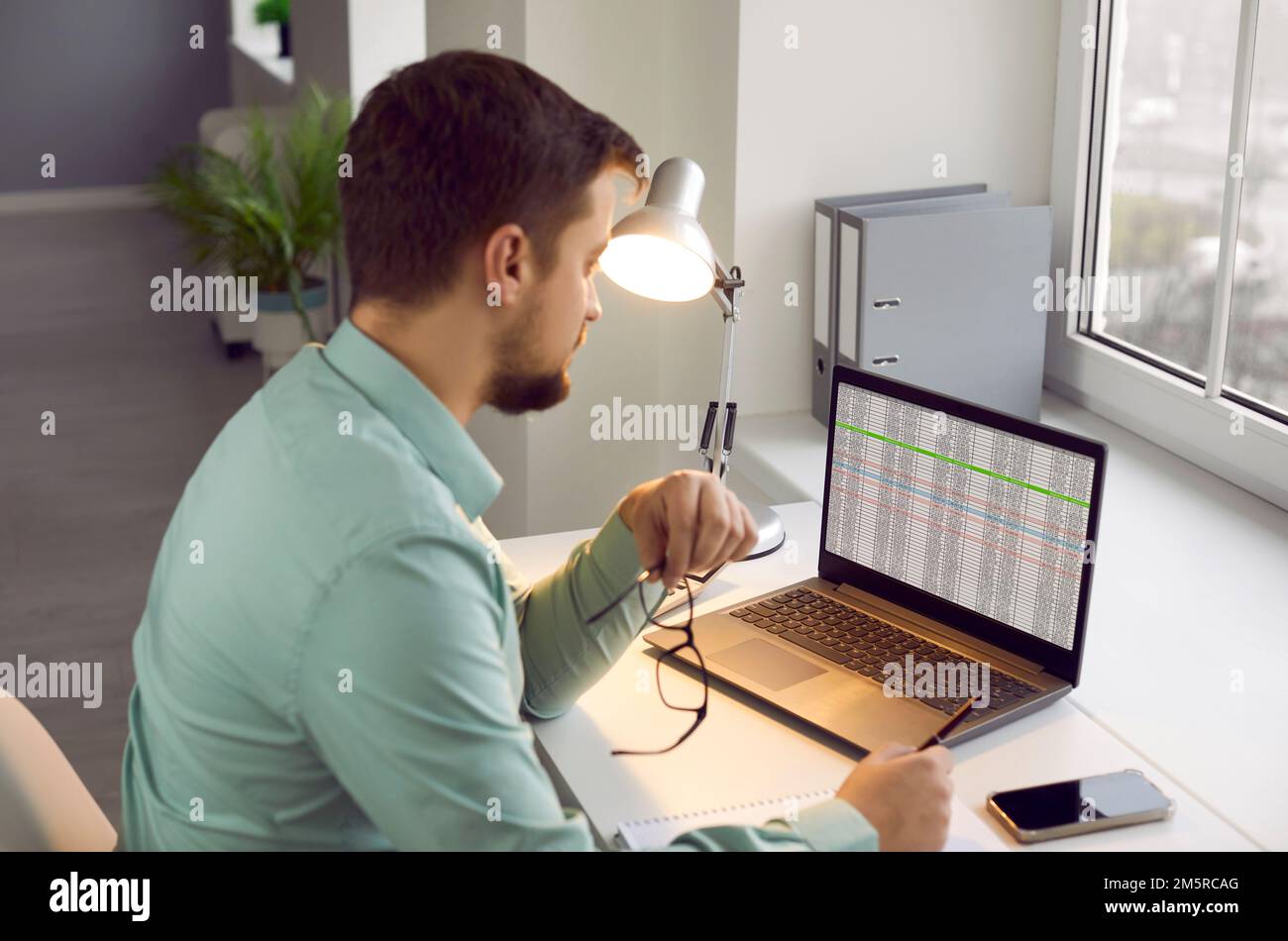 Der süße Kerl behält seine Brille, während er zu Hause mit seinem Laptop sitzt und gleichzeitig Remote arbeitet. Stockfoto