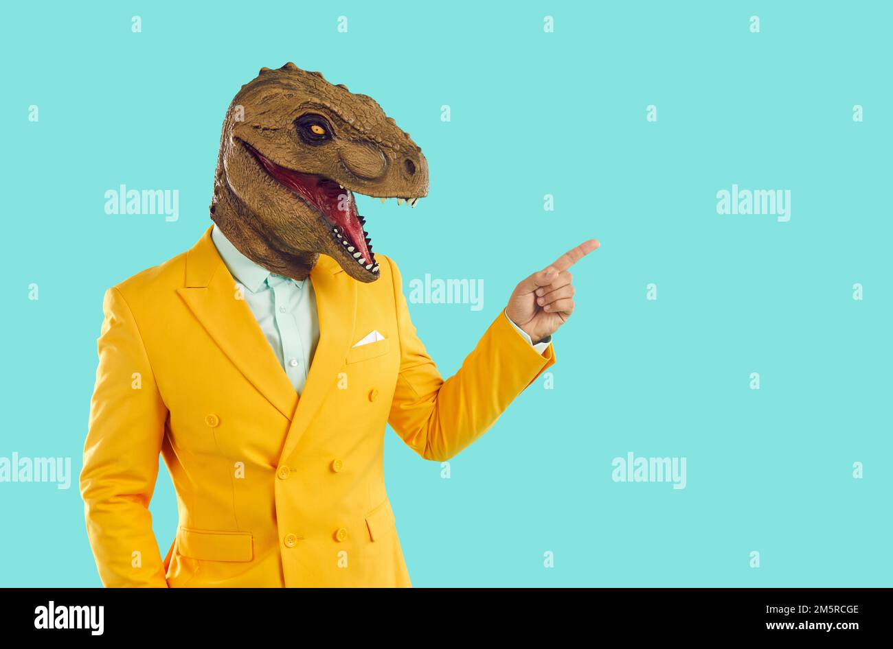 Ein cooler Mann in einer trendigen Gummi-Dinosaurier-Maske zeigt mit dem Finger auf die Stelle für Werbung. Stockfoto