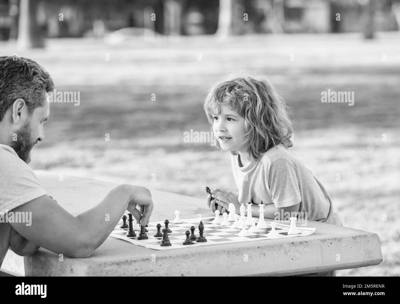 Glückliche Familie von Vater und Sohn Junge spielen Schach auf dem Tisch im Park im Freien, Schachwettbewerb Stockfoto
