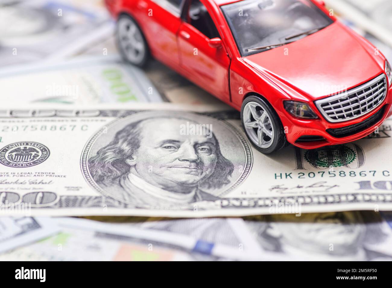 Rotes Spielzeugauto steht auf Dollar-Banknoten. Kosten für den Kauf eines Autos, Treibstoff Stockfoto