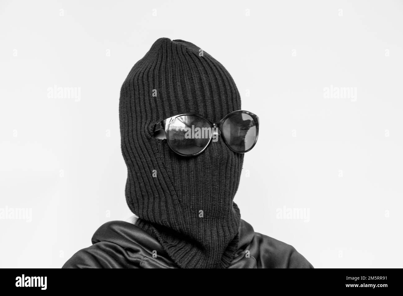 Hat Balaklava auf einem Mädchen und Sonnenbrille auf weißem Hintergrund, das Gesicht eines Diebes mit einem Hut mit einem Schlitz für Verben Stockfoto