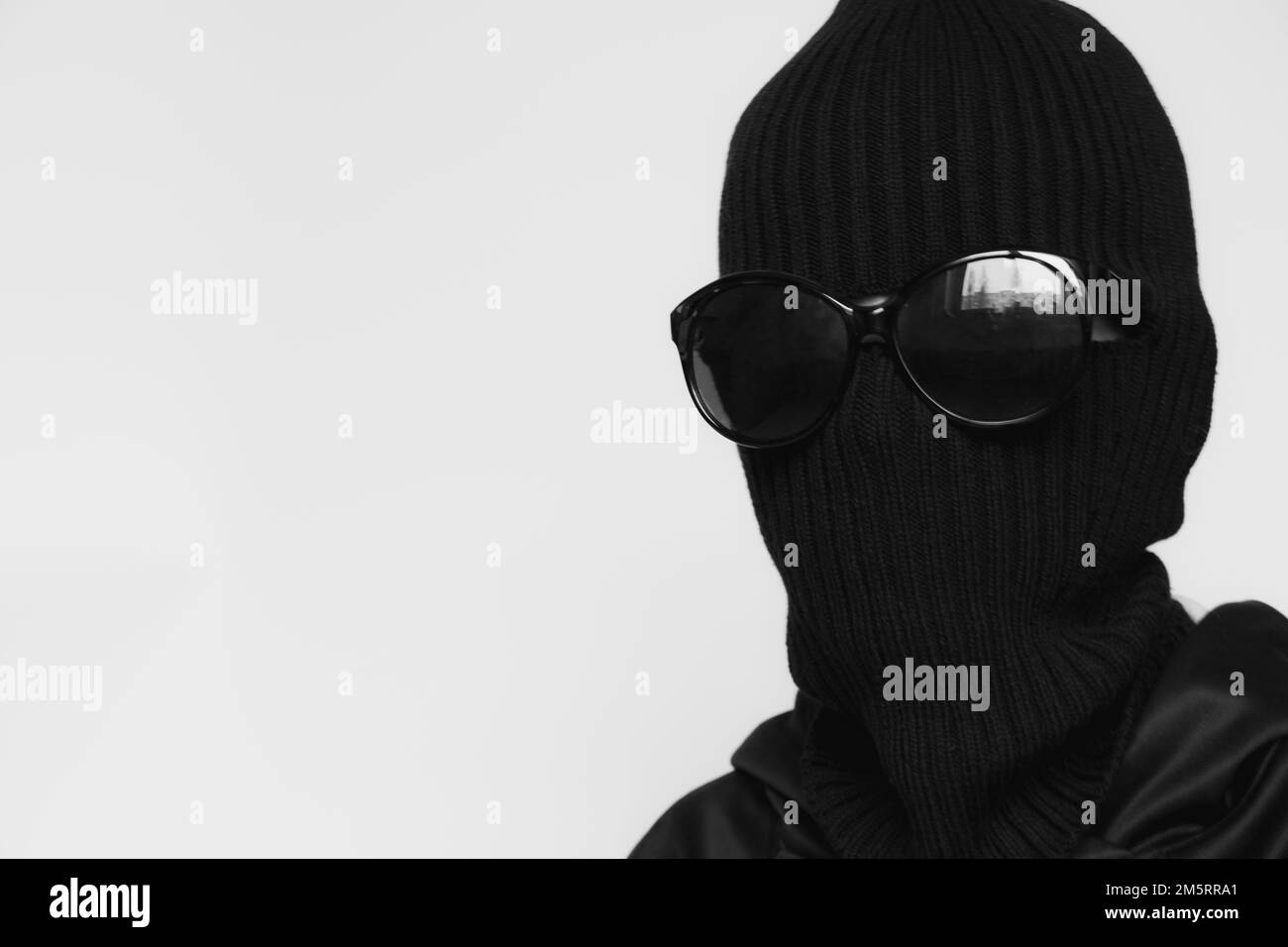 Hat Balaklava auf einem Mädchen und Sonnenbrille auf weißem Hintergrund, das Gesicht eines Diebes mit einem Hut mit einem Schlitz für Verben Stockfoto