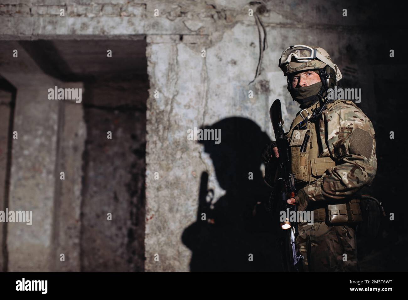 Porträt eines ukrainischen Verteidigers im Dugout. Ein Soldat mit einer Waffe in der Hand wirft einen Schatten auf die Wand. Stockfoto