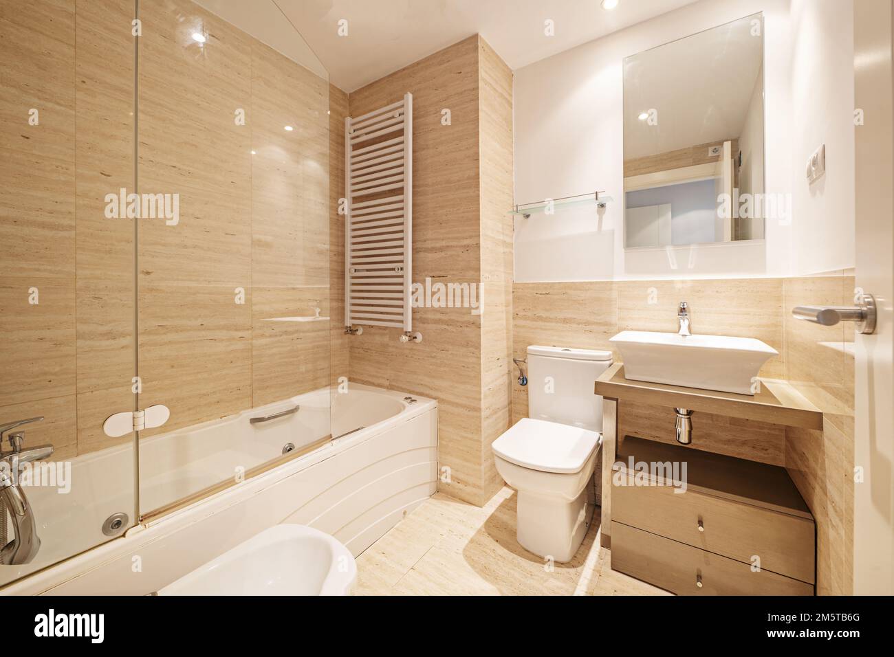 Badezimmer in konventionellem Design mit Marmorfliesen an Wänden und Böden, rechteckigem Spiegel, Schrank mit Schubladen und einem kleinen weißen Porzellanwaschbecken mit Koch Stockfoto