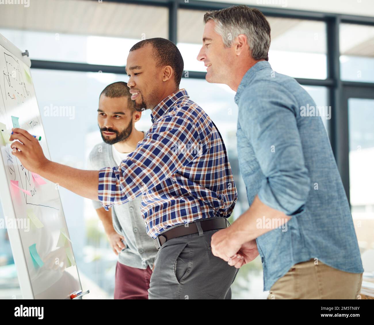 Große Köpfe machen die Arbeit einfach. Drei Geschäftsleute, die an einem Whiteboard arbeiten. Stockfoto