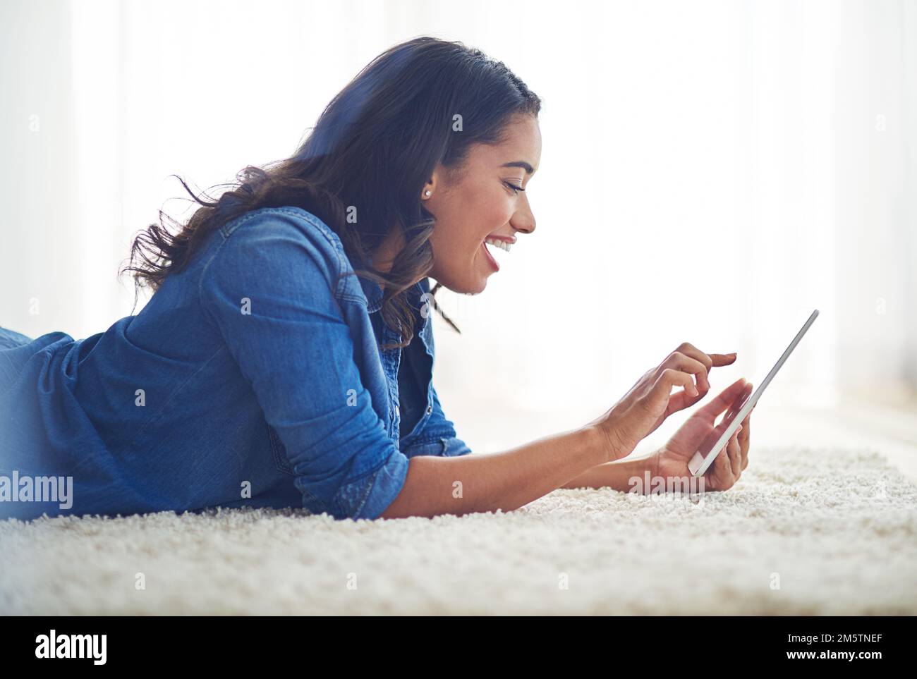 Eine Freundschaftsanfrage annehmen. Eine junge Frau, die zu Hause auf ihrem Tablet im Internet surft. Stockfoto