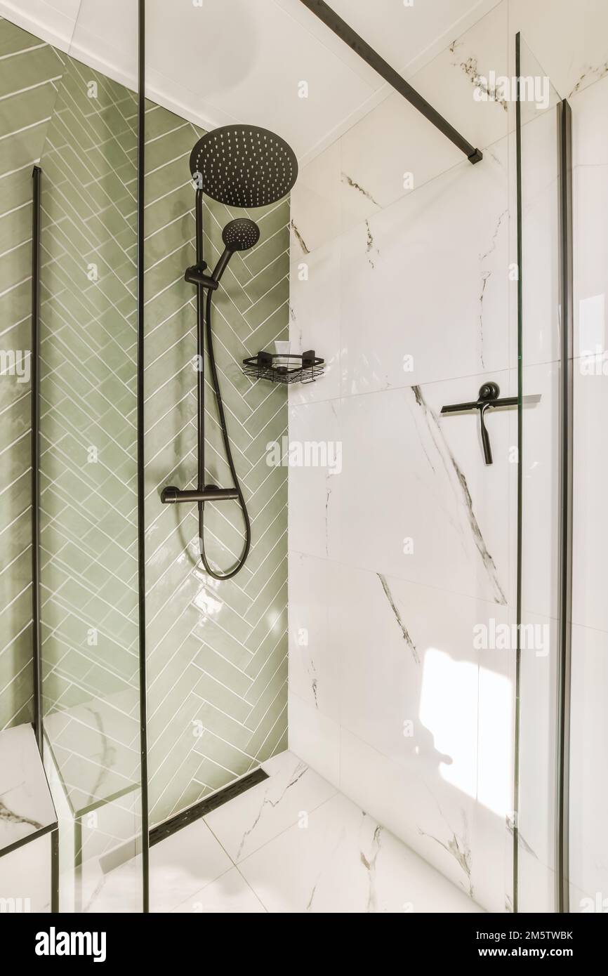 Ein Badezimmer mit grünen Fliesen und schwarzen Duschhähnen an der Wand daneben ist ein weiß gefliester Boden Stockfoto