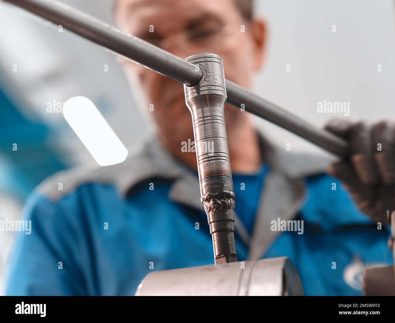 Porträt einer 50-55 Jahre alten Turner mit Brille bei der Arbeit. Bottom-up-Ansicht. Ältere Metallwender arbeiten in der Werkstatt an der Maschine hinter der Arbeit. Stockfoto