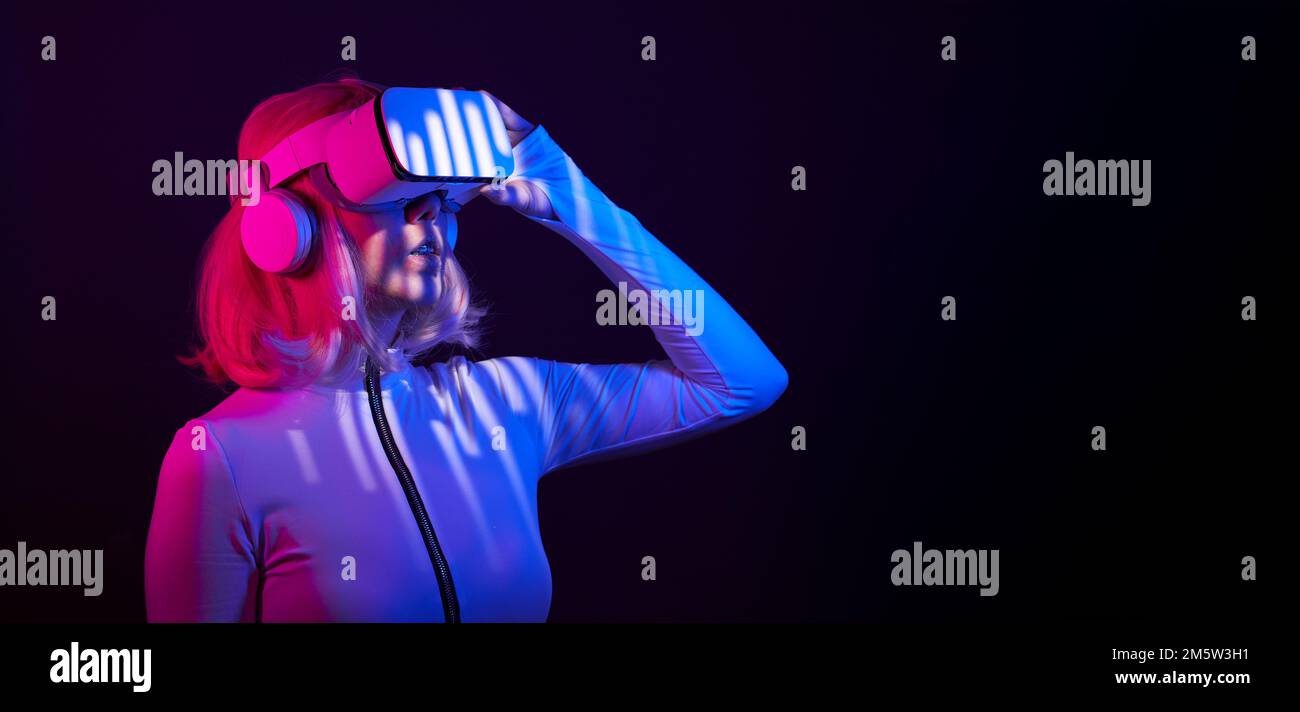 Eine Frau in Virtual-Reality-Brille in Neonfarben. Das Konzept der digitalen Technologie für Metaversum und Unterhaltung der Zukunft. Stockfoto