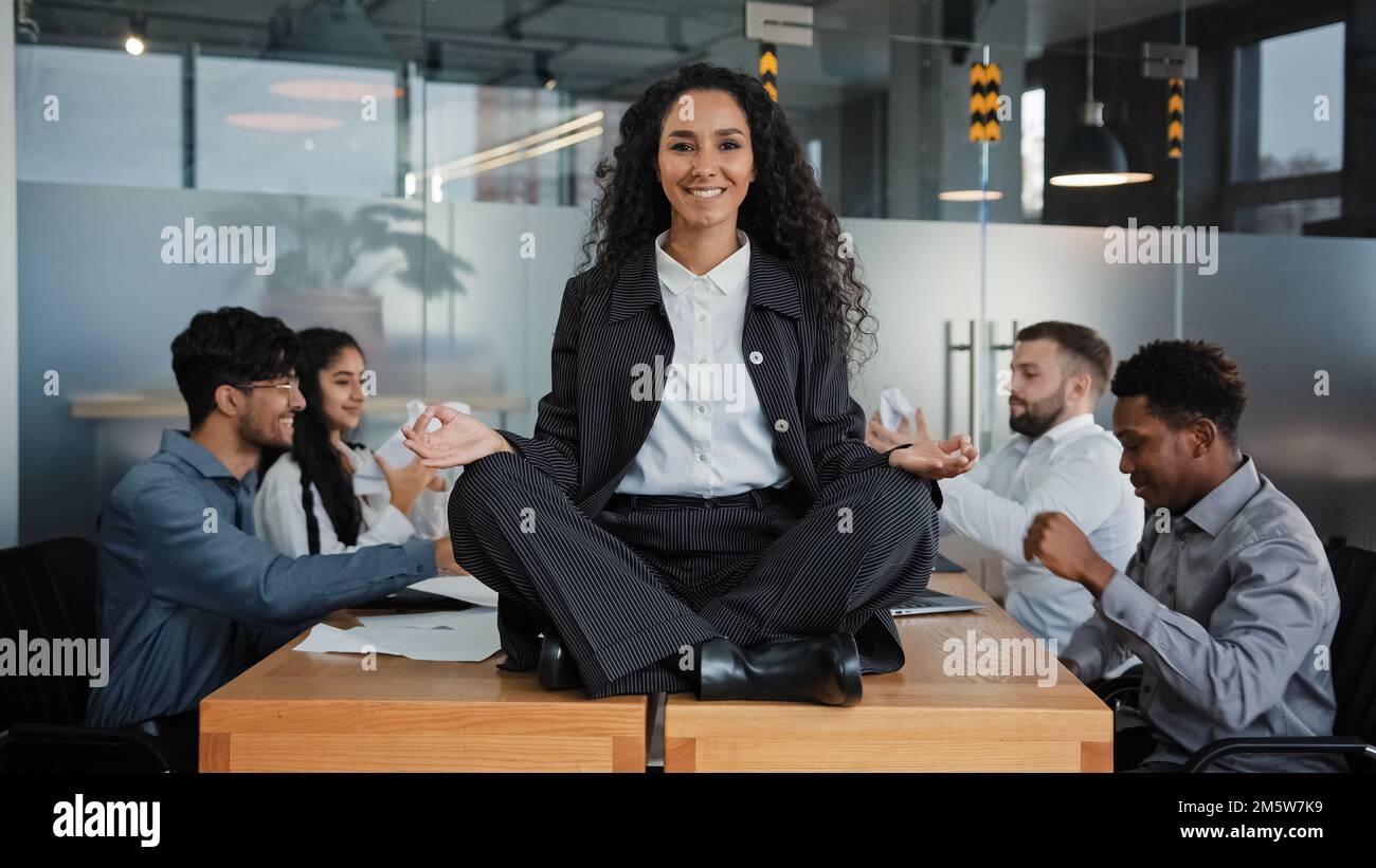Lächelnde Achtsamkeit Geschäftsfrau glückliche Anführerin, die an einem Tisch in Lotusposition sitzt und in einem Büro meditiert, entspannen im Meditationshintergrund Stockfoto